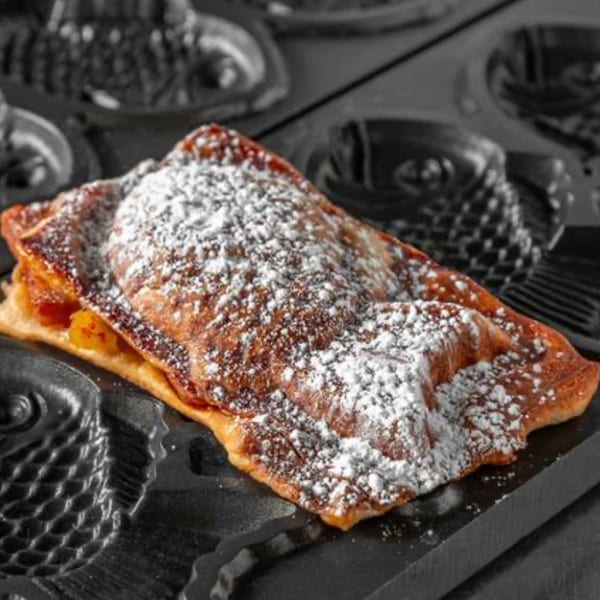 Freshly baked, golden-brown taiyaki dusted with powdered sugar, resting in a dark fish-shaped mold.
