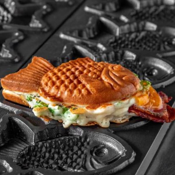 Savory taiyaki with melted cheese, green onions, and bacon, resting in a taiyaki iron.
