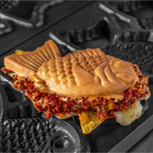 A savory taiyaki from BeanFish, filled with red toppings and melted cheese, rests in a dark waffle iron.