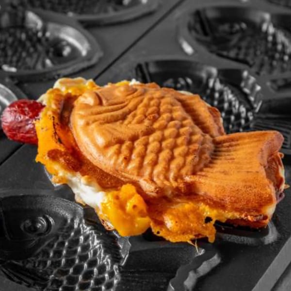 A golden-brown taiyaki waffle with a red filling and cheese, resting in a black fish-shaped mold.